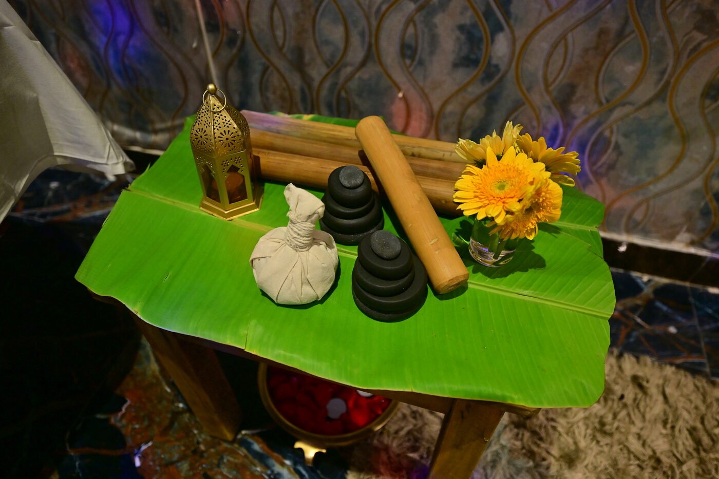 Spa treatment tools — herbal potli, hot stones, bamboo, and flowers on banana leaf at 111 Spa